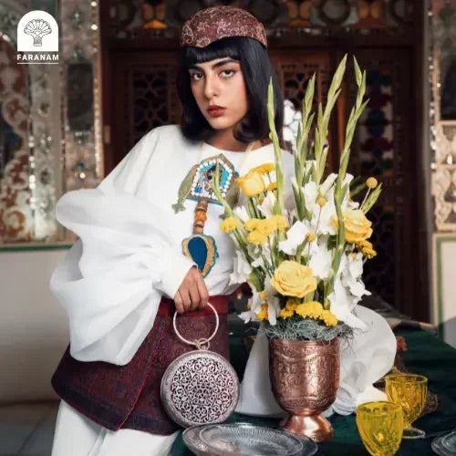 Woman holding a floral arrangement and a handbag in an ornate interior setting with 'FARANAM' branding.